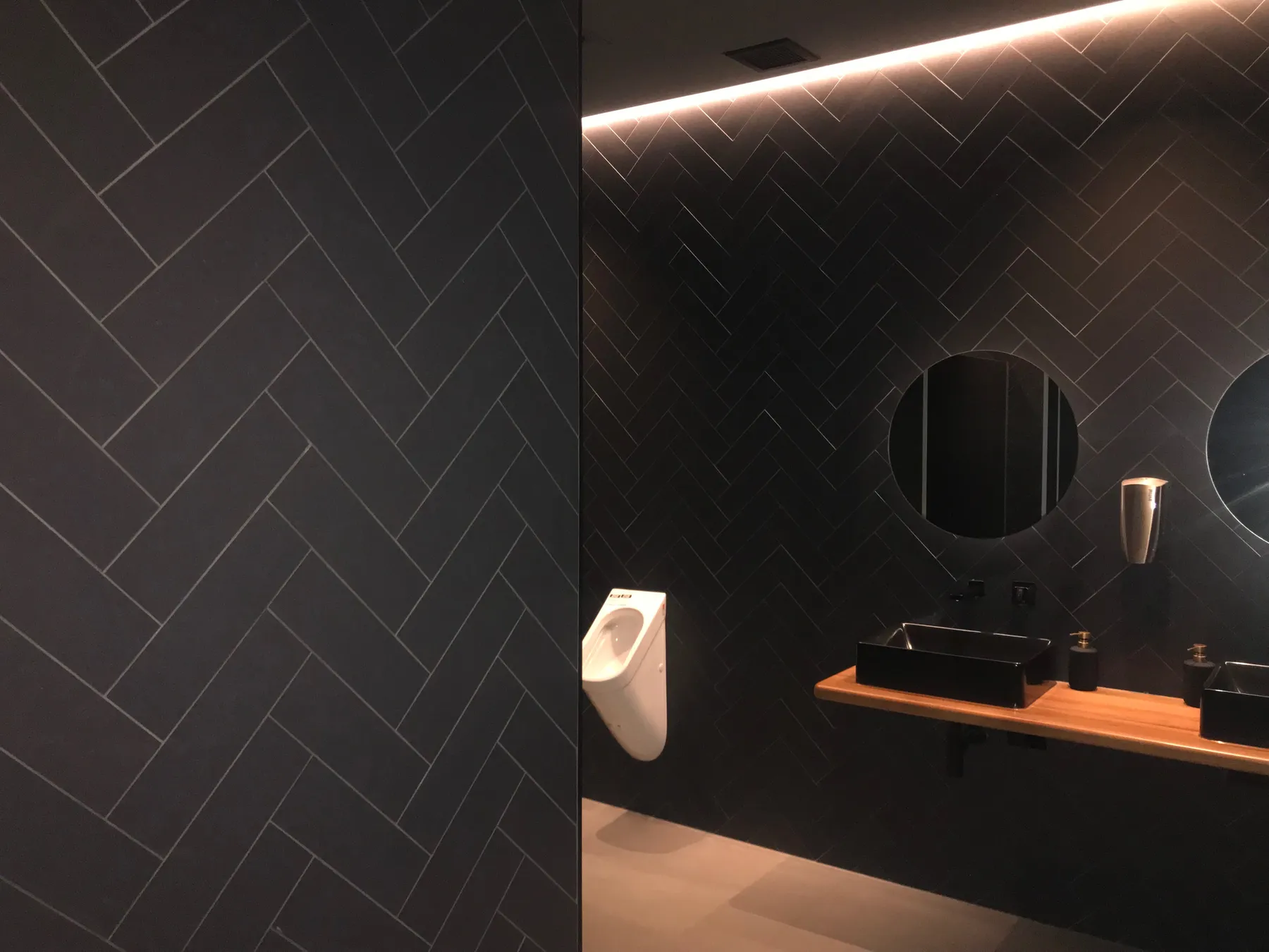 Commercial washroom with dark herringbone wall tiling by JSR Tiling